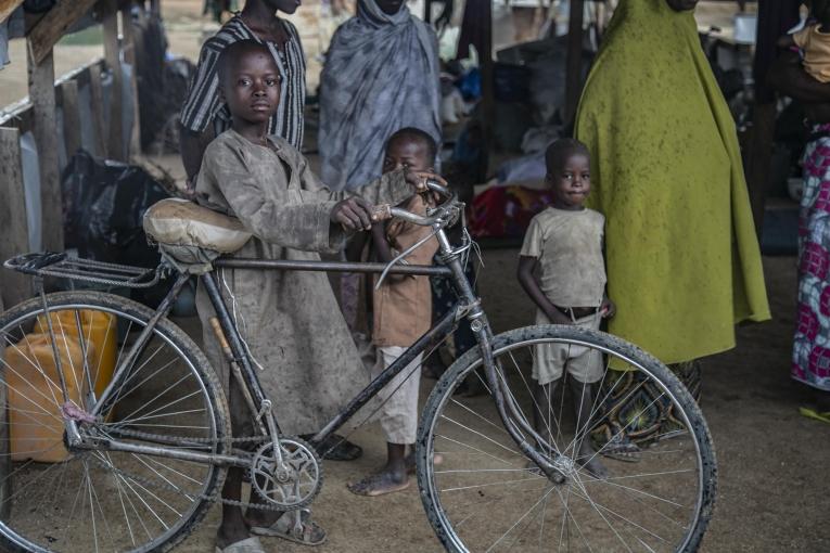 Un jeune garçon et sa bicyclette dans le camp de transit de la ville de Gwoza, où les personnes déplacées attendent de recevoir une tente familiale. 2018. Nigeria.