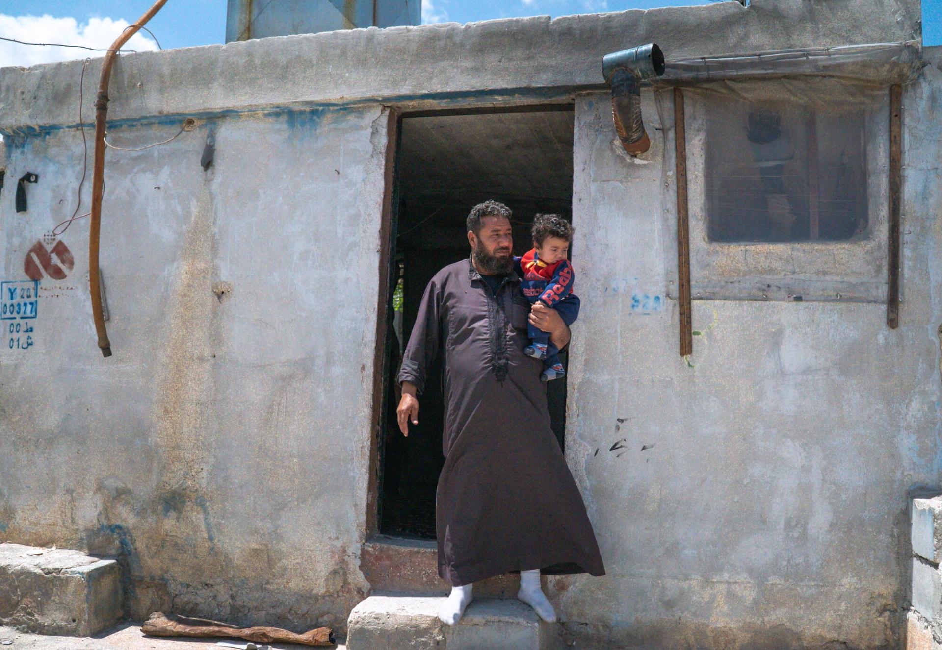 Walid et un de ses enfants devant son abri du camp d'Al-Kuwaiti, à Idlib.