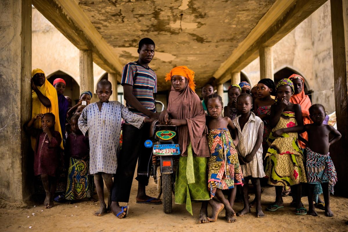 Des personnes déplacées dans la ville d'Anka. La jeune femme au foulard orange vivait à une journée de marche d'Anka avant l'attaque de son village. Elle habite dans un squat depuis un et demi avec ses parents et ses huit frères et sœurs. Nigeria. 2019.&nbsp;
 © Benedicte Kurzen/NOOR