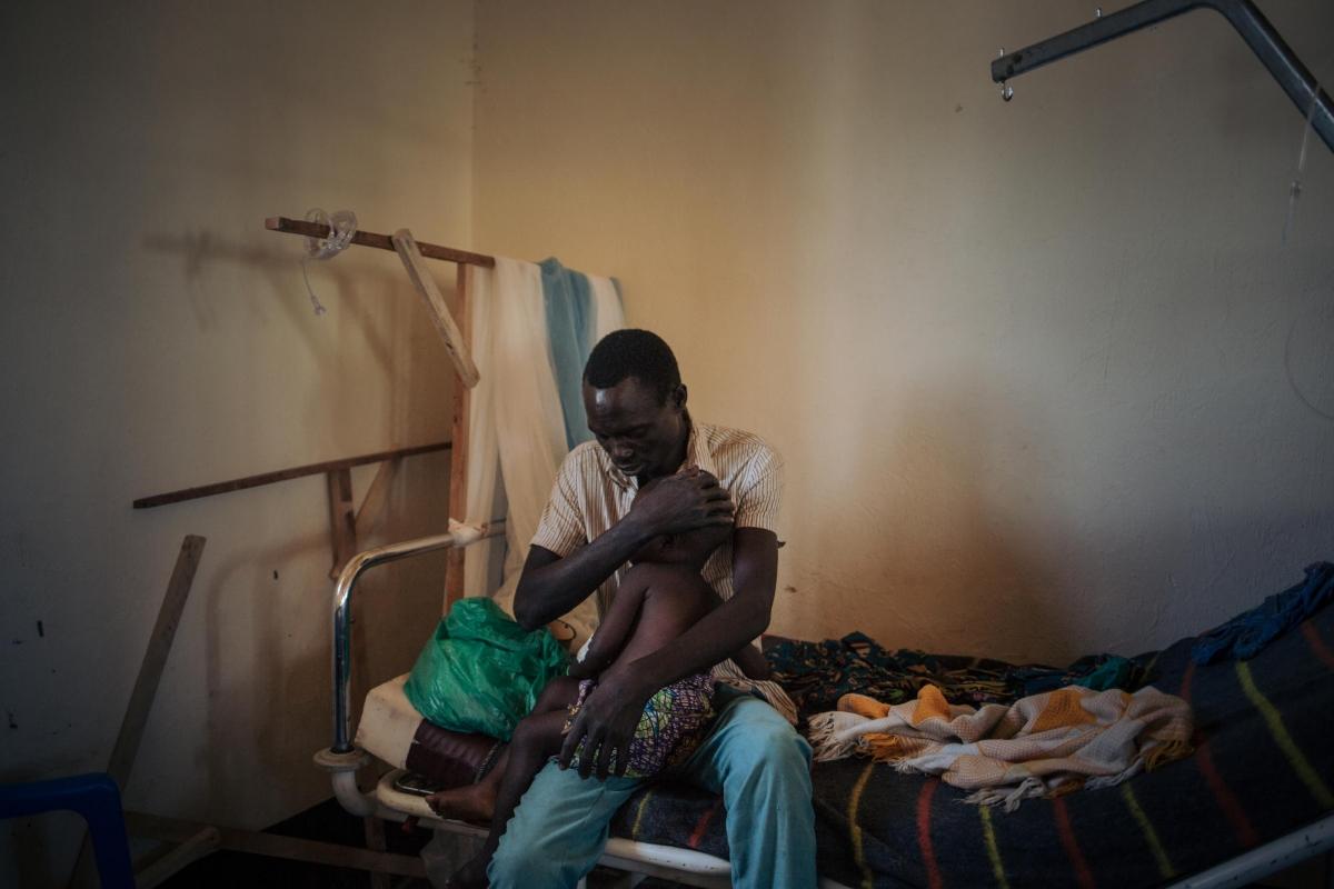 Un père tient sa fille de deux ans souffrant de la rougeole, dans l'unité de rougeole dirigée par MSF à l'hôpital de Biringi, dans la province d'Ituri, au Nord-Est de la République démocratique du Congo.
 © Alexis Huguet