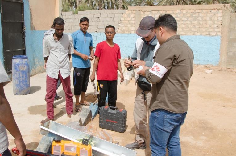 Une équipe de logisticiens MSF dans le centre de détention de Khoms est en train de fixer des lave-mains et échange avec les migrants qui sont détenus. Les conséquences médicales d’un mauvais accès à l’eau potable, telles que les diarrhées, sont parmi les principales pathologies vues en consultation dans les centres de Khoms et Misrata. 
 © Christophe Biteau/MSF