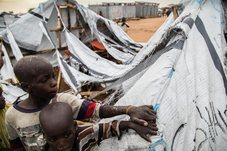 Deux enfants se tiennent devant un abri détruit dans le camp de transit de Pulka. 
 © Igor G. Barbero/MSF